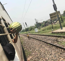 A guy bought this watermelon from a vendor while the train made a quick stop He had to hold it like this because it didnt fit between the bars and the train resumes its journey