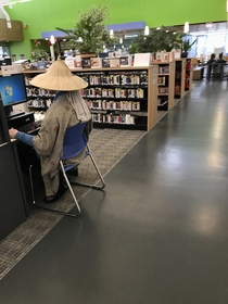 Dude casually wearing an asian rice hat in a library