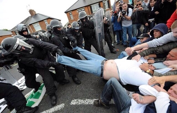 Police and rioters unite to help a fat dude out of his pants