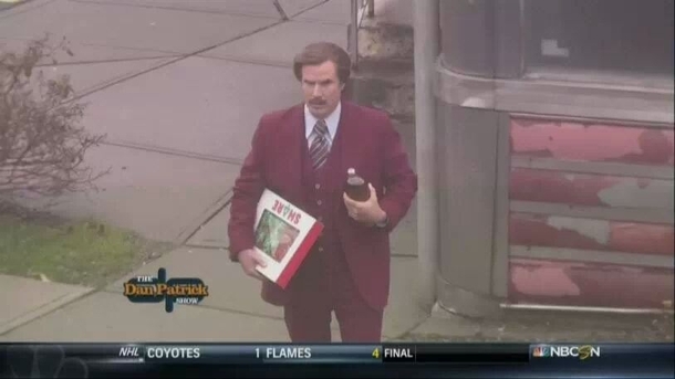 Ron Burgundy carrying a box of donuts and a  of Old English Lost in Millford looking for the ESPN studio