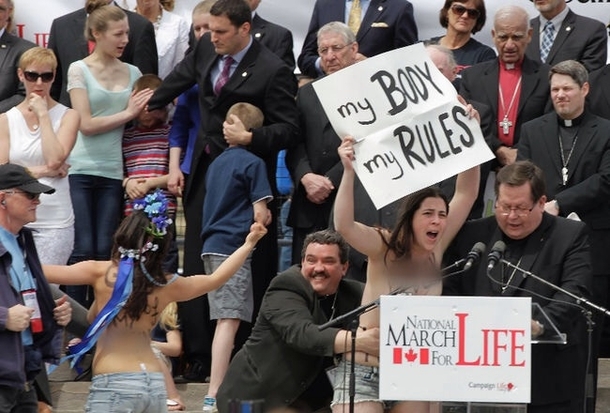 The guys face as he wrestles a topless protestor