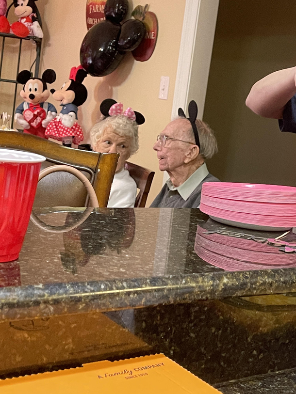 These two old people wearing mouse ears at a two year olds b day party