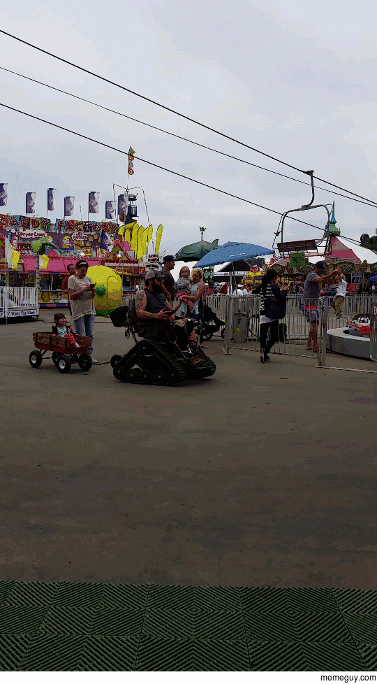 Wounded warrior on a tank track wheelchair towing child through the fair We salute you