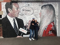 Jerry Seinfeld in front of a mural of himself rejecting Keshas hug