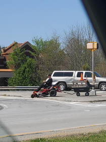 Just a man in a suit driving through the city on his lawn mower