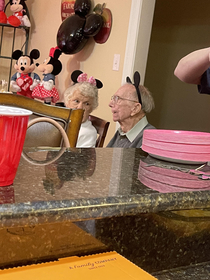 These two old people wearing mouse ears at a two year olds b day party