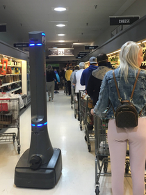 This photo from a grocery store makes it look like humans are being patrolled by a social distance enforcement robot